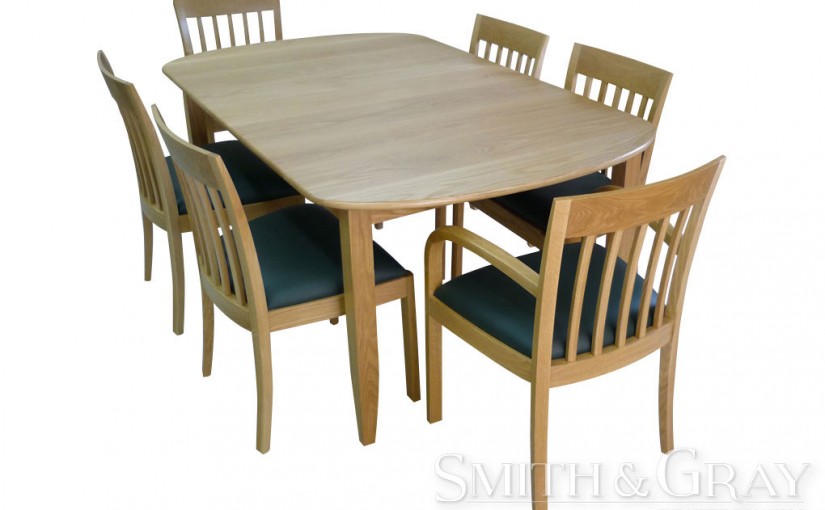 Modern dining suite table with rounded ends tapered legs and 2 chairs with curved timber arm and flared legs in American Oak